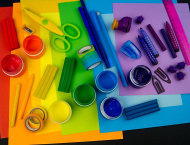 Okul aksesuarları gökkuşağı şeklinde ortaya konur. Siyah arka plan. Okul öğrencisine mutlu. Çocuklar için sanat ve el sanatları. Gökkuşağı renkleri, alfabe harfleri ve sayıları öğrenen çocuk.