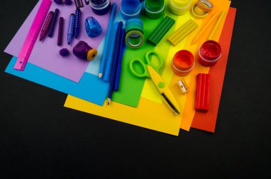 Okul aksesuarları gökkuşağı şeklinde ortaya konur. Siyah arka plan. Okul öğrencisine mutlu. Çocuklar için sanat ve el sanatları. Gökkuşağı renkleri, alfabe harfleri ve sayıları öğrenen çocuk.