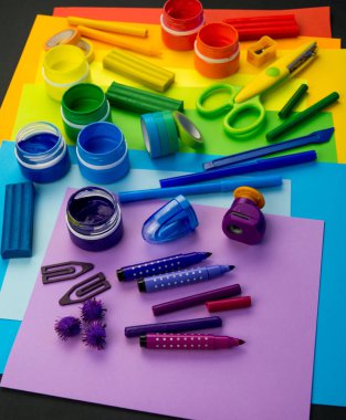 Okul aksesuarları gökkuşağı şeklinde ortaya konur. Siyah arka plan. Okul öğrencisine mutlu. Çocuklar için sanat ve el sanatları. Gökkuşağı renkleri, alfabe harfleri ve sayıları öğrenen çocuk.