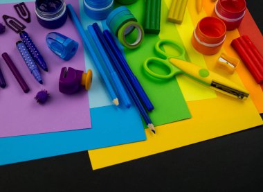 Okul aksesuarları gökkuşağı şeklinde ortaya konur. Siyah arka plan. Okul öğrencisine mutlu. Çocuklar için sanat ve el sanatları. Gökkuşağı renkleri, alfabe harfleri ve sayıları öğrenen çocuk.