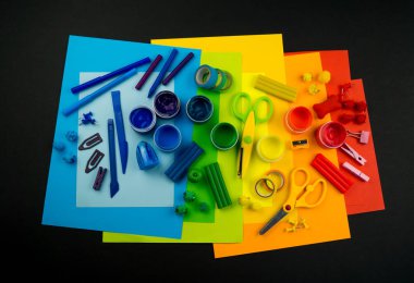 Okul aksesuarları gökkuşağı şeklinde ortaya konur. Siyah arka plan. Okul öğrencisine mutlu. Çocuklar için sanat ve el sanatları. Gökkuşağı renkleri, alfabe harfleri ve sayıları öğrenen çocuk.