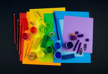 Okul aksesuarları gökkuşağı şeklinde ortaya konur. Siyah arka plan. Okul öğrencisine mutlu. Çocuklar için sanat ve el sanatları. Gökkuşağı renkleri, alfabe harfleri ve sayıları öğrenen çocuk.