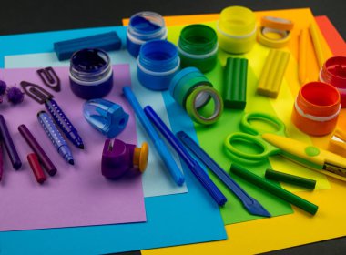 Okul aksesuarları gökkuşağı şeklinde ortaya konur. Siyah arka plan. Okul öğrencisine mutlu. Çocuklar için sanat ve el sanatları. Gökkuşağı renkleri, alfabe harfleri ve sayıları öğrenen çocuk.