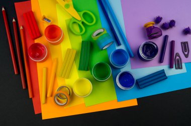 Okul aksesuarları gökkuşağı şeklinde ortaya konur. Siyah arka plan. Okul öğrencisine mutlu. Çocuklar için sanat ve el sanatları. Gökkuşağı renkleri, alfabe harfleri ve sayıları öğrenen çocuk.