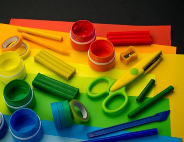 Okul aksesuarları gökkuşağı şeklinde ortaya konur. Siyah arka plan. Okul öğrencisine mutlu. Çocuklar için sanat ve el sanatları. Gökkuşağı renkleri, alfabe harfleri ve sayıları öğrenen çocuk.