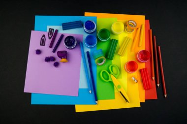 Okul aksesuarları gökkuşağı şeklinde ortaya konur. Siyah arka plan. Okul öğrencisine mutlu. Çocuklar için sanat ve el sanatları. Gökkuşağı renkleri, alfabe harfleri ve sayıları öğrenen çocuk.