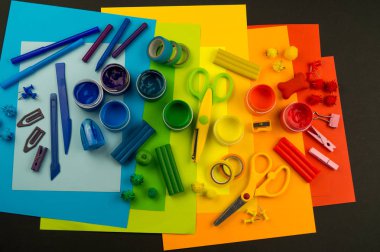 Okul aksesuarları gökkuşağı şeklinde ortaya konur. Siyah arka plan. Okul öğrencisine mutlu. Çocuklar için sanat ve el sanatları. Gökkuşağı renkleri, alfabe harfleri ve sayıları öğrenen çocuk.