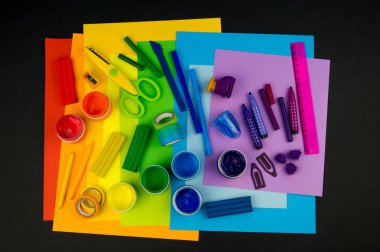 Okul aksesuarları gökkuşağı şeklinde ortaya konur. Siyah arka plan. Okul öğrencisine mutlu. Çocuklar için sanat ve el sanatları. Gökkuşağı renkleri, alfabe harfleri ve sayıları öğrenen çocuk.