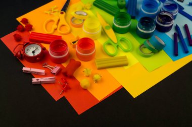 Okul aksesuarları gökkuşağı şeklinde ortaya konur. Siyah arka plan. Okul öğrencisine mutlu. Çocuklar için sanat ve el sanatları. Gökkuşağı renkleri, alfabe harfleri ve sayıları öğrenen çocuk.