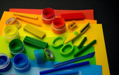 Okul aksesuarları gökkuşağı şeklinde ortaya konur. Siyah arka plan. Okul öğrencisine mutlu. Çocuklar için sanat ve el sanatları. Gökkuşağı renkleri, alfabe harfleri ve sayıları öğrenen çocuk.