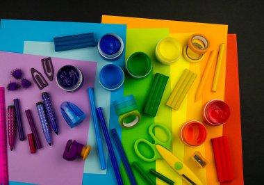 Okul aksesuarları gökkuşağı şeklinde ortaya konur. Siyah arka plan. Okul öğrencisine mutlu. Çocuklar için sanat ve el sanatları. Gökkuşağı renkleri, alfabe harfleri ve sayıları öğrenen çocuk.