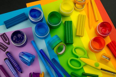 Okul aksesuarları gökkuşağı şeklinde ortaya konur. Siyah arka plan. Okul öğrencisine mutlu. Çocuklar için sanat ve el sanatları. Gökkuşağı renkleri, alfabe harfleri ve sayıları öğrenen çocuk.