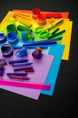 Okul aksesuarları gökkuşağı şeklinde ortaya konur. Siyah arka plan. Okul öğrencisine mutlu. Çocuklar için sanat ve el sanatları. Gökkuşağı renkleri, alfabe harfleri ve sayıları öğrenen çocuk.