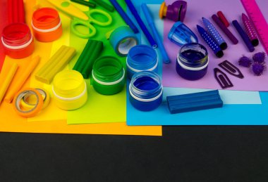 Okul aksesuarları gökkuşağı şeklinde ortaya konur. Siyah arka plan. Okul öğrencisine mutlu. Çocuklar için sanat ve el sanatları. Gökkuşağı renkleri, alfabe harfleri ve sayıları öğrenen çocuk.