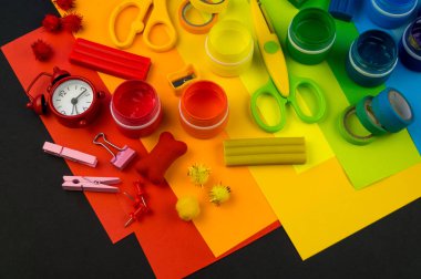 Okul aksesuarları gökkuşağı şeklinde ortaya konur. Siyah arka plan. Okul öğrencisine mutlu. Çocuklar için sanat ve el sanatları. Gökkuşağı renkleri, alfabe harfleri ve sayıları öğrenen çocuk.