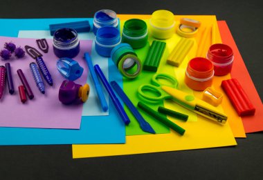 Okul aksesuarları gökkuşağı şeklinde ortaya konur. Siyah arka plan. Okul öğrencisine mutlu. Çocuklar için sanat ve el sanatları. Gökkuşağı renkleri, alfabe harfleri ve sayıları öğrenen çocuk.