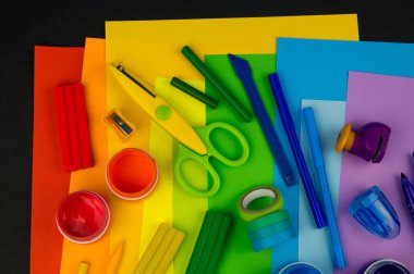 Okul aksesuarları gökkuşağı şeklinde ortaya konur. Siyah arka plan. Okul öğrencisine mutlu. Çocuklar için sanat ve el sanatları. Gökkuşağı renkleri, alfabe harfleri ve sayıları öğrenen çocuk.