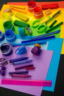 Okul aksesuarları gökkuşağı şeklinde ortaya konur. Siyah arka plan. Okul öğrencisine mutlu. Çocuklar için sanat ve el sanatları. Gökkuşağı renkleri, alfabe harfleri ve sayıları öğrenen çocuk.