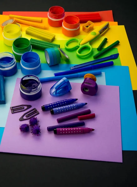 Okul aksesuarları gökkuşağı şeklinde ortaya konur. Siyah arka plan. Okul öğrencisine mutlu. Çocuklar için sanat ve el sanatları. Gökkuşağı renkleri, alfabe harfleri ve sayıları öğrenen çocuk.