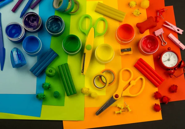 Okul aksesuarları gökkuşağı şeklinde ortaya konur. Siyah arka plan. Okul öğrencisine mutlu. Çocuklar için sanat ve el sanatları. Gökkuşağı renkleri, alfabe harfleri ve sayıları öğrenen çocuk.