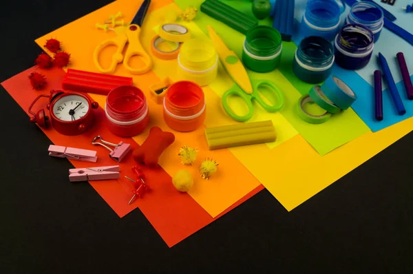 Okul aksesuarları gökkuşağı şeklinde ortaya konur. Siyah arka plan. Okul öğrencisine mutlu. Çocuklar için sanat ve el sanatları. Gökkuşağı renkleri, alfabe harfleri ve sayıları öğrenen çocuk.