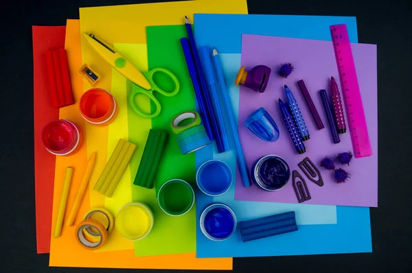 Okul aksesuarları gökkuşağı şeklinde ortaya konur. Siyah arka plan. Okul öğrencisine mutlu. Çocuklar için sanat ve el sanatları. Gökkuşağı renkleri, alfabe harfleri ve sayıları öğrenen çocuk.