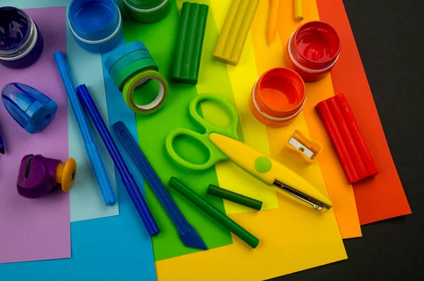 Okul aksesuarları gökkuşağı şeklinde ortaya konur. Siyah arka plan. Okul öğrencisine mutlu. Çocuklar için sanat ve el sanatları. Gökkuşağı renkleri, alfabe harfleri ve sayıları öğrenen çocuk.