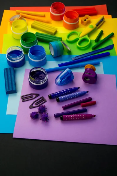 Okul aksesuarları gökkuşağı şeklinde ortaya konur. Siyah arka plan. Okul öğrencisine mutlu. Çocuklar için sanat ve el sanatları. Gökkuşağı renkleri, alfabe harfleri ve sayıları öğrenen çocuk.