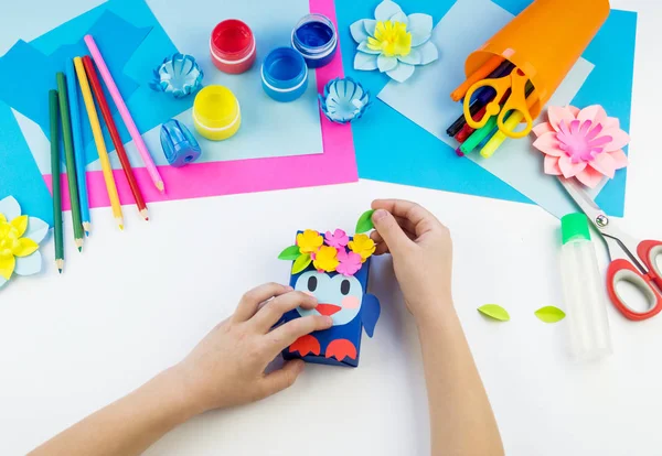 Çocuk elleri kağıttan penguen yapıyor. Çocukların yaratıcılığının uygulanması. Anaokulu ve zanaat okulu. Beyaz arka plan ve el sanatları için malzemeler.