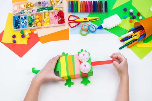 Kind bastelt ein Hackbox-Chamäleon. Material für Kreativität auf weißem Hintergrund. — Stockfoto