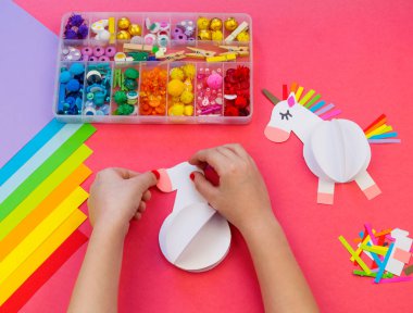 Pembe bir arka plan üzerinde kağıttan yapılmış tek boynuzlu at. Çocukların elleri el sanatları yapmak.