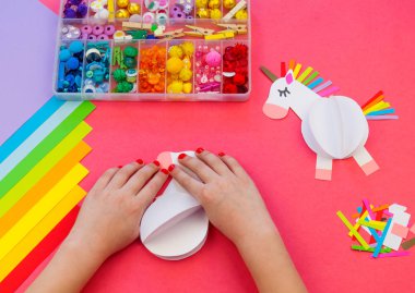 Pembe bir arka plan üzerinde kağıttan yapılmış tek boynuzlu at. Çocukların elleri el sanatları yapmak.