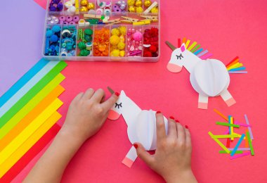 Pembe bir arka plan üzerinde kağıttan yapılmış tek boynuzlu at. Çocukların elleri el sanatları yapmak.