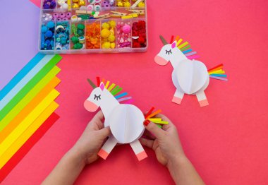 Pembe bir arka plan üzerinde kağıttan yapılmış tek boynuzlu at. Çocukların elleri el sanatları yapmak.