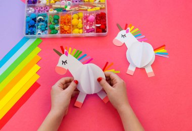 Pembe bir arka plan üzerinde kağıttan yapılmış tek boynuzlu at. Çocukların elleri el sanatları yapmak.