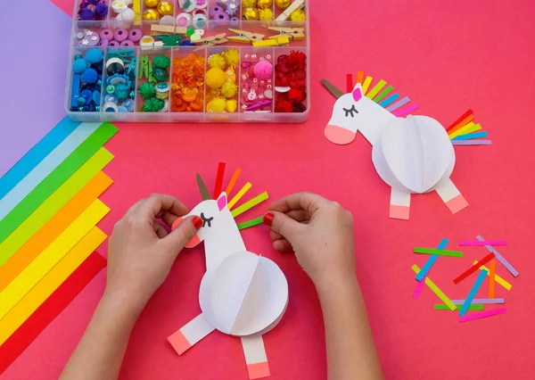 Licorne en papier sur fond rose. Les mains des enfants font de l'artisanat . — Photo