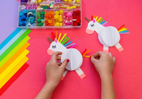 Pembe bir arka plan üzerinde kağıttan yapılmış tek boynuzlu at. Çocukların elleri el sanatları yapmak.