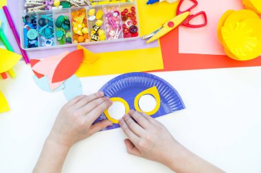 Bir çocuk kağıttan kuş maskesi yapar. Usta sınıf el sanatları. Tropikal Papağan.