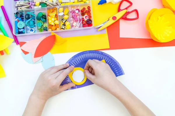 Un niño hace una máscara de pájaro de papel. Artesanía de clase magistral. Loro tropical . — Foto de Stock