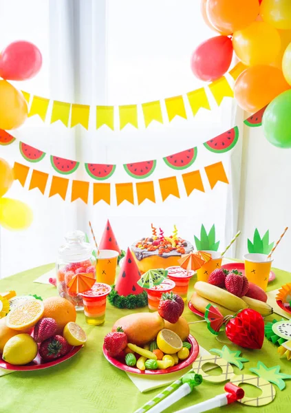 Decoración para unas vacaciones de cumpleaños de los niños. Fiesta de frutas. Pastel y dulces dulces. Vajilla desechable y frutas tropicales . — Foto de Stock