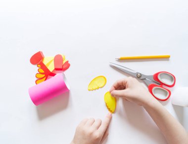 Çocuk kartondan bir zanaat yapar. Kağıt papağan pembesi. Eller kızlar.