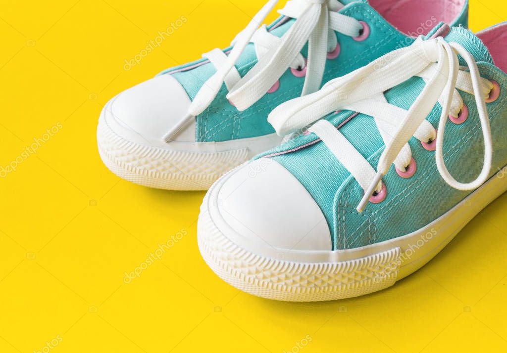 New turquoise sneakers on yellow background with copy space.
