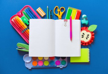 Açık bir not defteri mavi bir arka plan üzerinde yer alır. Ofis malzemeleri etrafında gökkuşağının rengi vardır.