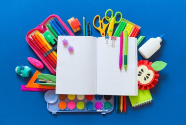 Açık bir not defteri mavi bir arka plan üzerinde yer alır. Ofis malzemeleri etrafında gökkuşağının rengi vardır.