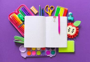 Açık bir not defteri Violet arka plan üzerinde yatıyor. Ofis malzemeleri etrafında gökkuşağının rengi vardır.