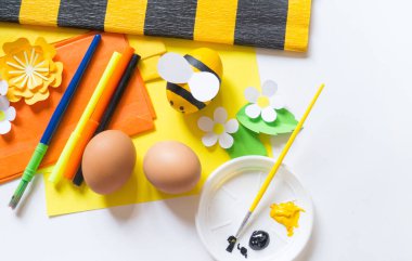 Çocuk elleri kız paskalya yumurtası boyar. Yumurta sarı bir arı. Beyaz arka plan. Yaratıcılık için malzeme,