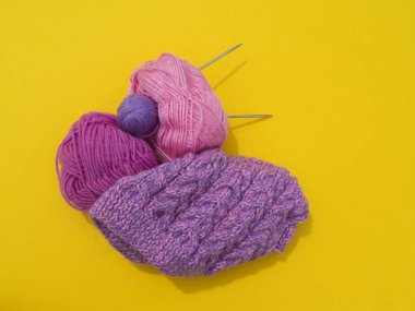 Yün pembe ve mor kat lar bağlantısız bir kapağın yanında yer almakta. Sarı arka plan.