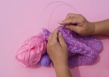 Kadının elleri mor iplik bir kap örgü. Pembe arka plan