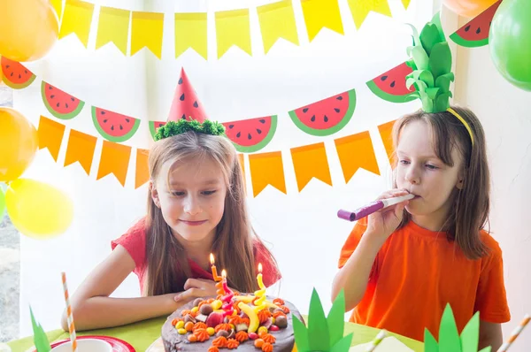 Las chicas celebran su cumpleaños. El niño apaga las velas del pastel. Fiesta de frutas. Piña y sandía . — Foto de Stock