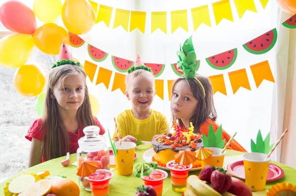 Los niños celebran un cumpleaños. El niño apaga las velas del pastel. Fiesta de frutas . —  Fotos de Stock